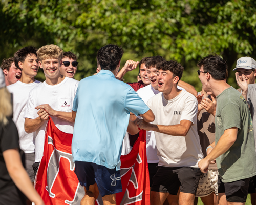 A group of young men performs a synchronized dance outdoors, wearing black-and-white striped shirts, denim shorts, and white sneakers.